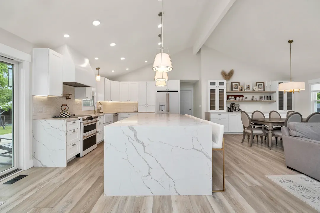 Open-plan white kitchen with a marble waterfall island and pendant lights