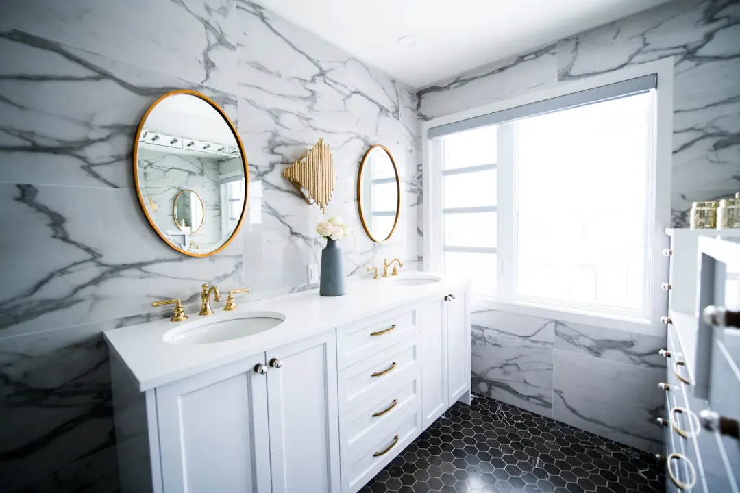 Small marble bathroom with round mirrors and a white vanity
