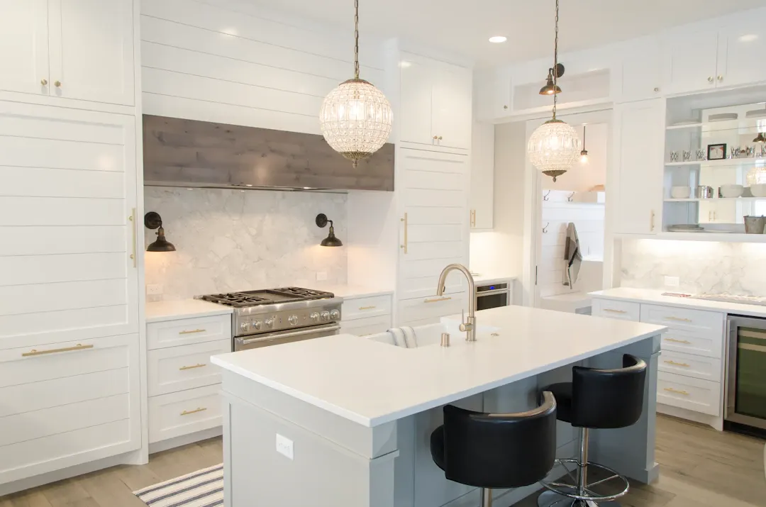 White kitchen with a plaster range hood, island seating and a glass pendant